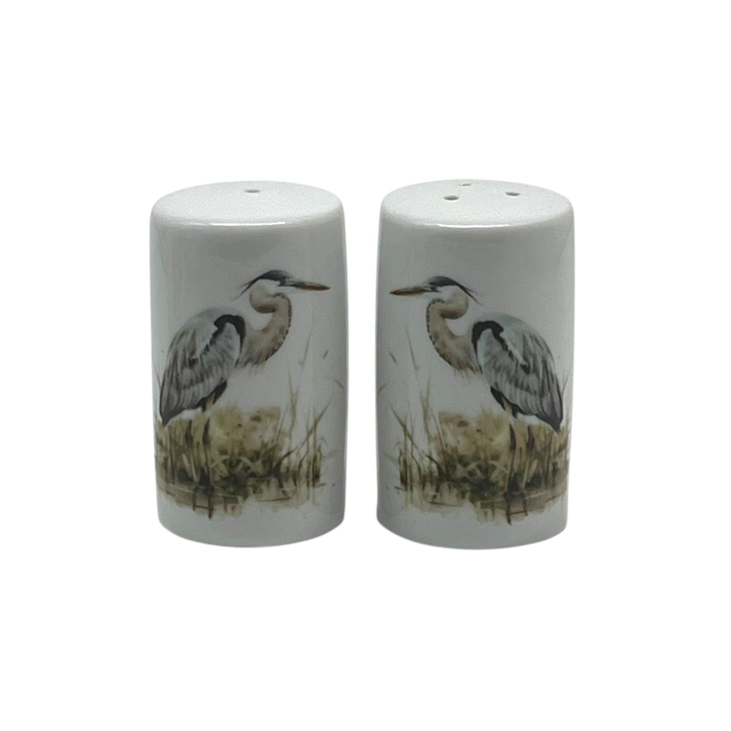 Pair of cylindrical white porcelain salt and pepper shakers featuring blue herons standing among softly painted marsh reeds.