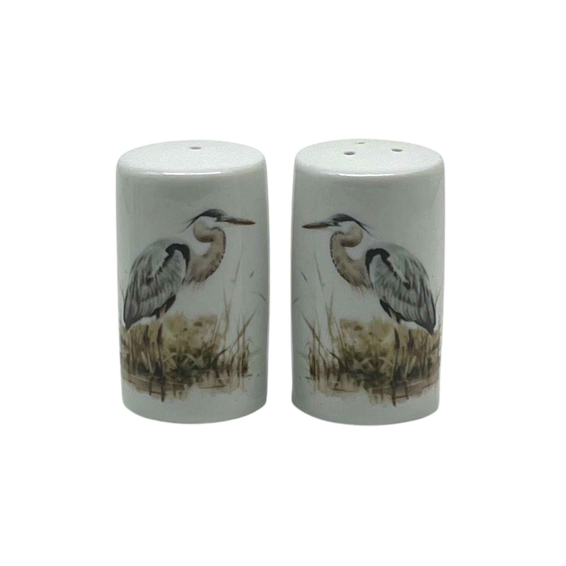 Pair of cylindrical white porcelain salt and pepper shakers featuring blue herons standing among softly painted marsh reeds.
