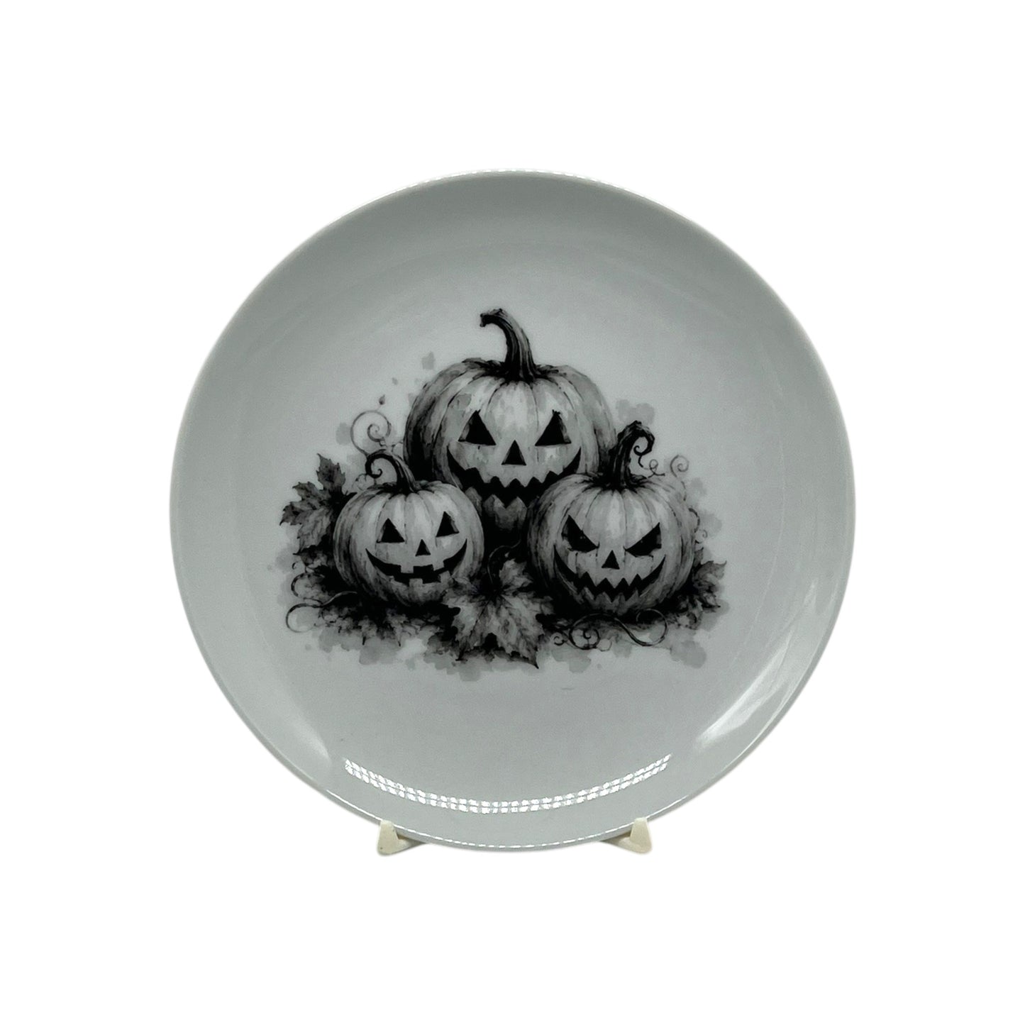 Shop the 6.25" Jack-O’-Lantern Trio Halloween Coupe Plate featuring three carved pumpkins in striking black-and-white artwork. Perfect for spooky entertaining.